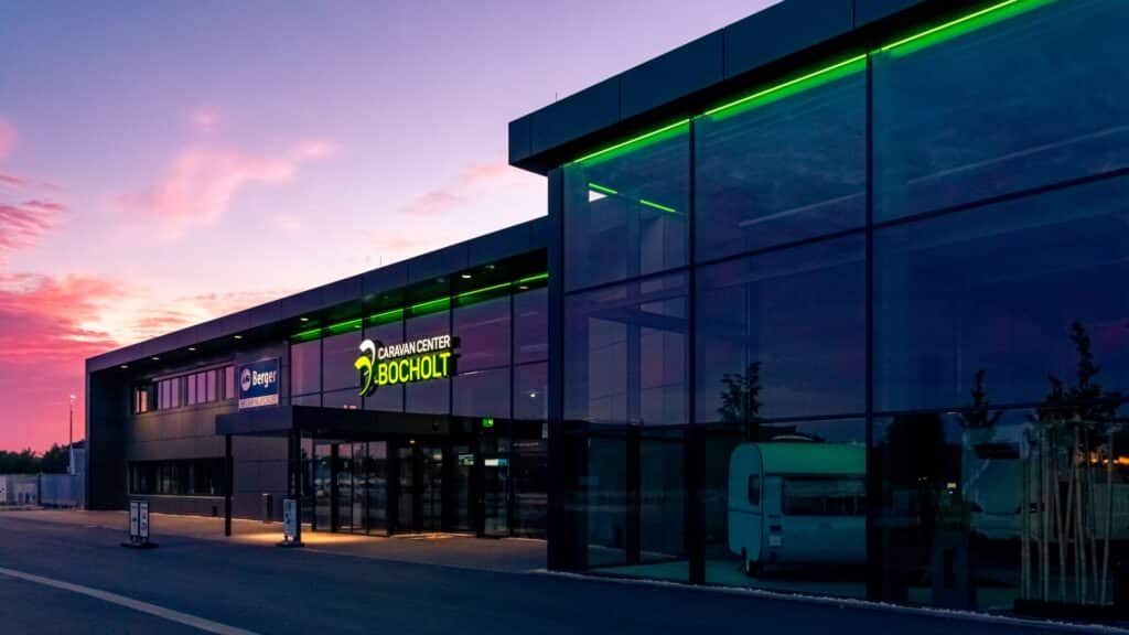 Beleuchteter Eingangsbereich des Caravan Center Bocholt mit großer Glasfront in der Abenddämmerung.