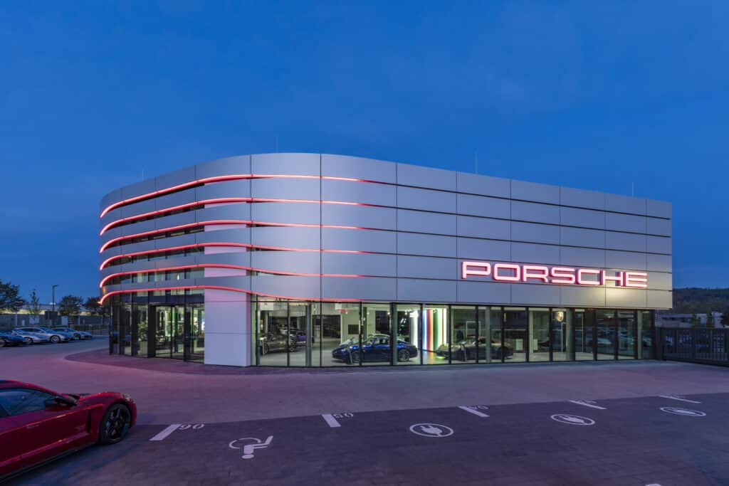 Außenansicht des Porsche Zentrums Karlsruhe in der Abenddämmerung mit rot beleuchteter Fassade und Porsche-Logo.