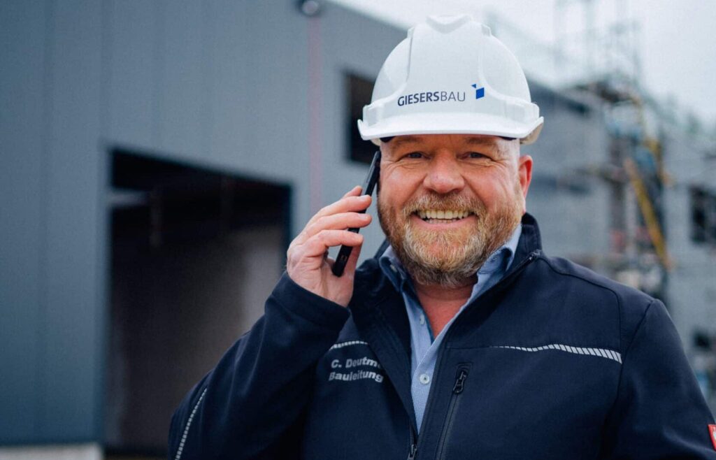 Giesers Bau MItarbeiter mit Helm telefonierend auf der Baustelle