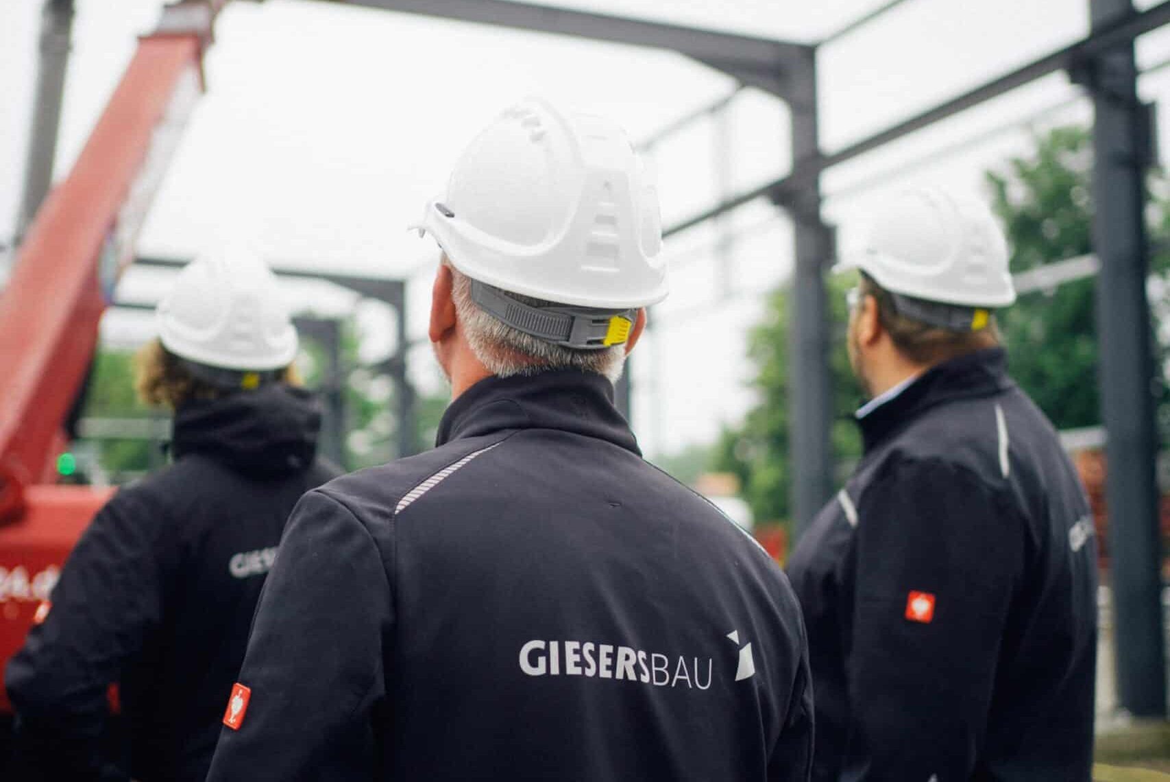 Mitarbeitende von Giesers Stahlbau GmbH die mit dem Rücken zur Kamera stehen auf einer Baustelle