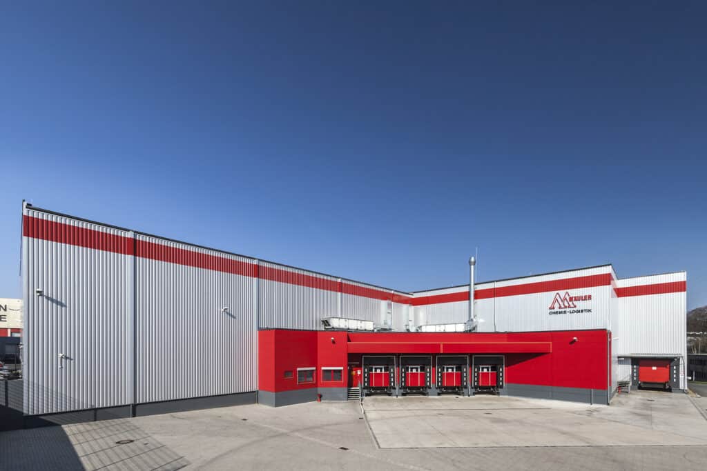 Große Lagerhalle in Remscheid mit markanter rot-silberner Fassade und mehreren überdachten Ladepunkten im Verladebereich. Im Vordergrund befindet sich eine weitläufige, gepflasterte Hoffläche.